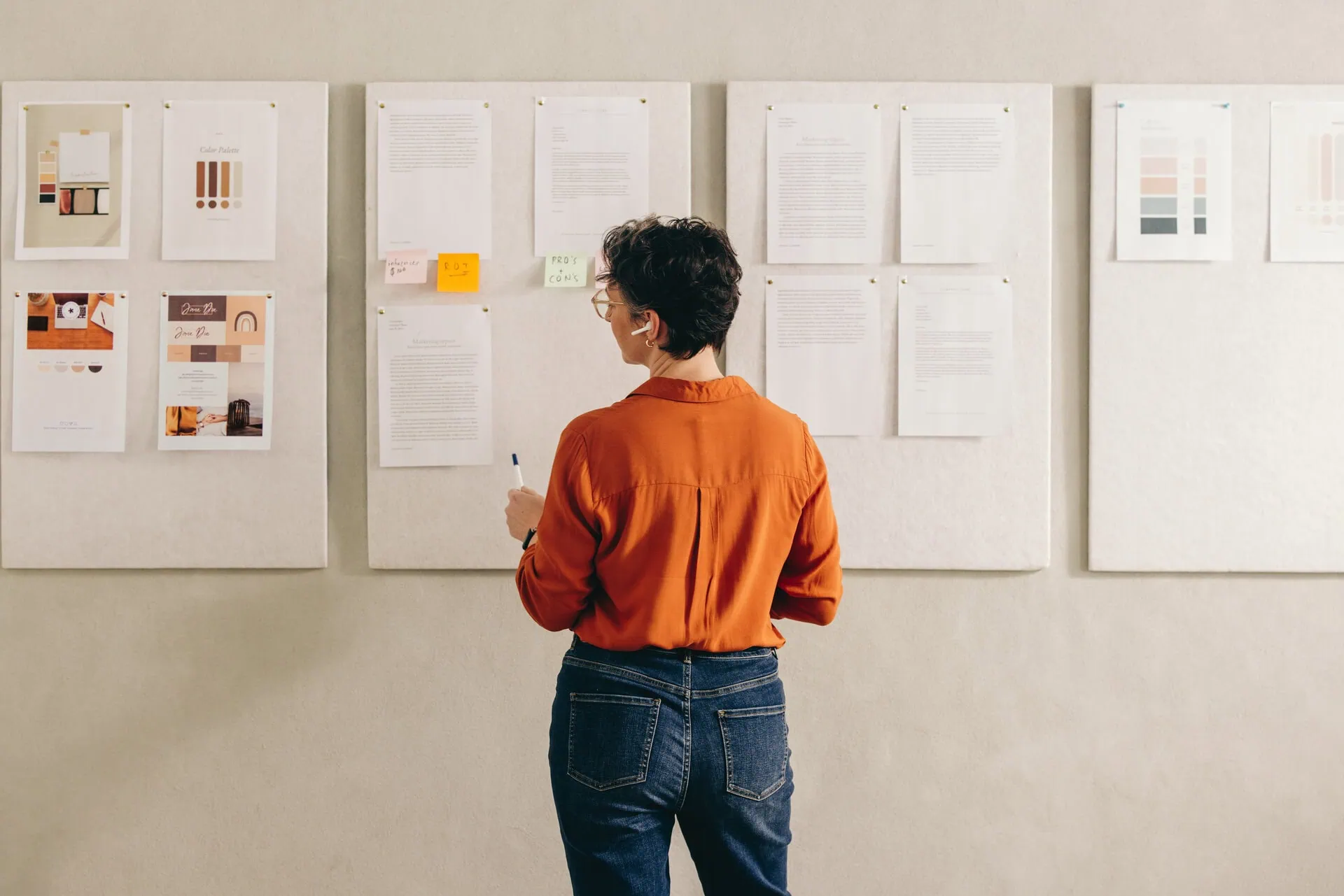 Woman in an orange top looking at brand strategy workshop sheets on a wall